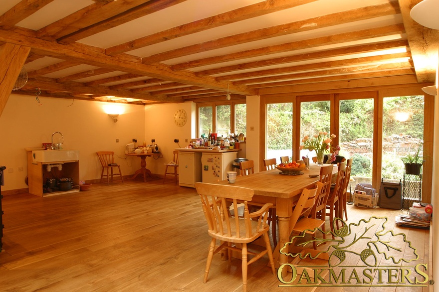Modern kitchen extension with simple exposed beams and oak frame patio doors leading to country house garden