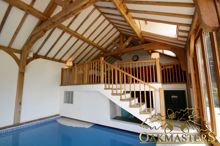 Oak frame stairs lead to gallery seating area in poolhouse