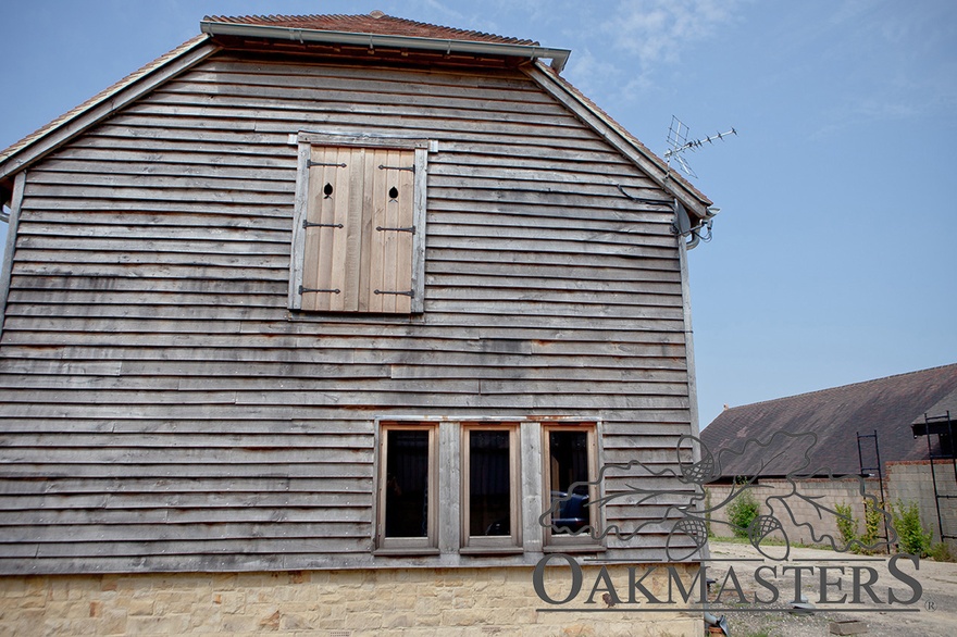 Side of the oak-clad barn with window and shutter detail