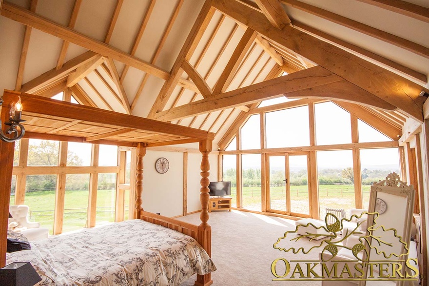 Exposed oak truss and rafters on vaulted ceiling in country house bedroom with glazed gable