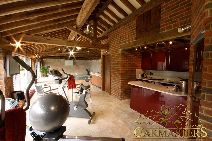 Brick walled kitchen area beneath exposed oak vaulted ceiling of oak and stone gym