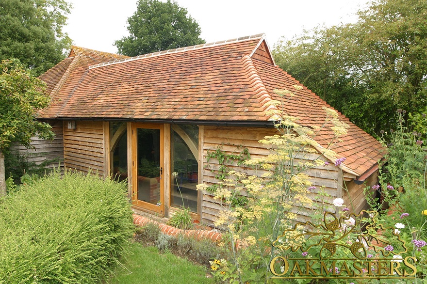 Oak frame glazed door framed with curved braces on oak clad garden room with catslide roof