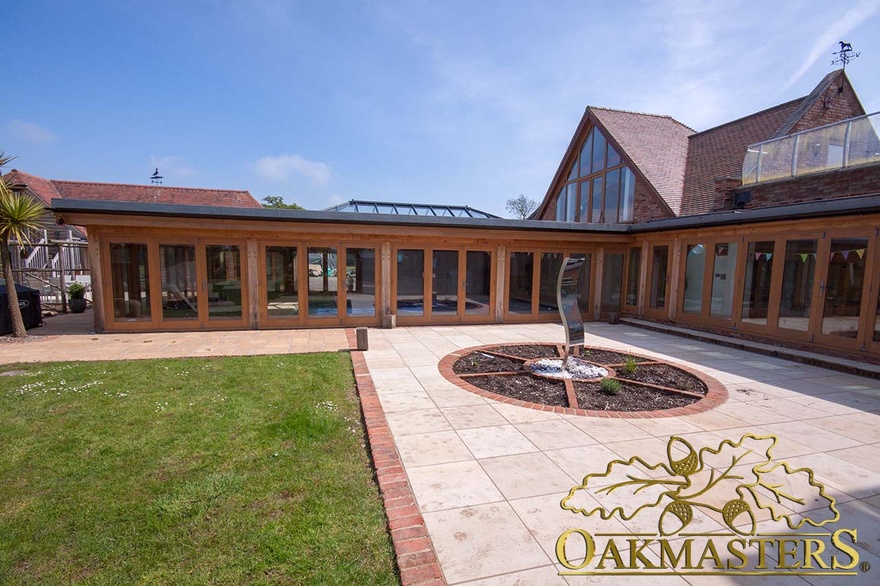 The oak framed swimming pool house with the flat roof extends the house beautifully